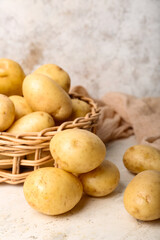 Wicker bowl with raw potatoes on white table