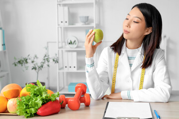 Female Asian nutritionist with apple at table in office