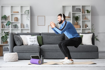Sporty young man in headphones exercising on yoga mat at home