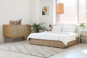 Interior of light bedroom with tables, palm tree and drawers