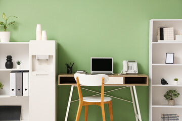 Interior of stylish office with modern water cooler, workspace and shelving unit