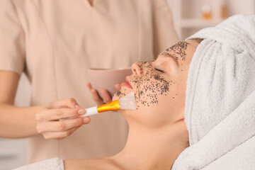 Young woman receiving chia seeds face mask on couch in beauty salon, closeup