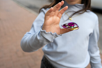 A child is skillfully spinning a vibrant spinner while standing on a sidewalk. The scene captures the joy of outdoor play during the day, showcasing a moment of concentration.