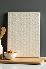 Cream-colored textured tile leaning against a dark gray wall, a wooden cutting board, and a small bowl of crumbs.