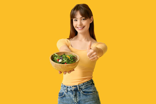Young woman with fresh vegetable salad on yellow background