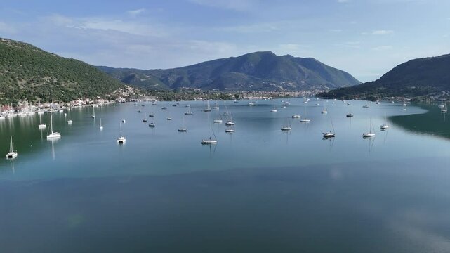 A side aerial view of sailing holiday yachts moored in a natural sheltered sea bay of a Greek island.