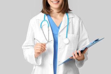Happy female cardiologist with stethoscope and clipboard on grey background, closeup