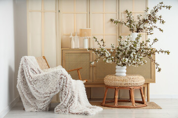 Interior of stylish living room with armchair, folding screen, commode and blooming branches in...