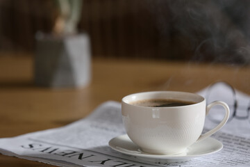 Newspaper with cup of coffee on table against blurred background, closeup