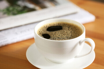 Newspaper with cup of coffee on table, closeup