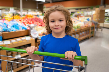 Kid with shopping cart at grocery store. Shopping with kids. Kid buying fruit in supermarket. Little boy buy fresh vegetables in grocery store. Kid choosing vegetables. Healthy food.