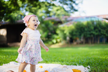 Happy toddler girl enjoys leisure time outdoors on picnic blanket surrounded by nature with family nearby, capturing joyful concept of people spending quality time together