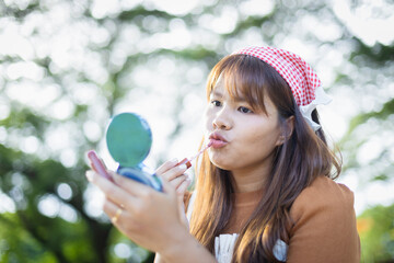 Young woman applies makeup outdoors during family picnic, enjoying leisure time with people around in natural setting that captures concept of relaxation and self care