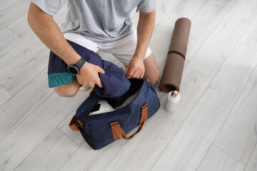 Young man putting jacket into sports bag at gym