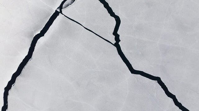 Drone flight over intricate pattern of cracks on the icy surface of frozen lake