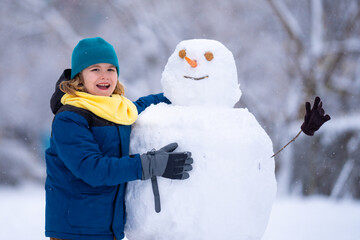 Kid play with snowman in winter. Snowman with a carrot nose on a winters day. Child making snowman. Little boy building snowball for funny snowman in snowy winter park. Snowmen in a snowy winter park.