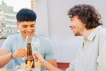 Homosexual couple of Latin, sitting and laughing, proudly toast on outdoor rooftop