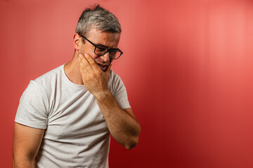 Man holding his face in discomfort against a red background
