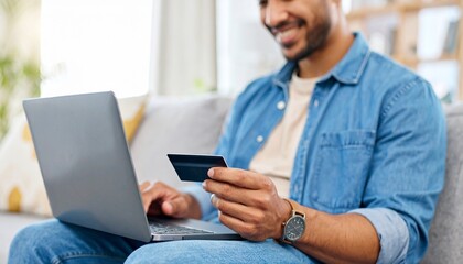 Smiling man using a laptop to do online shopping and holding a credit card