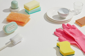 Colorful sponges, brushes, and gloves placed beside a few dishes, highlighting household cleaning...