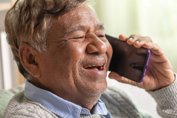 Cheerful old man laughs while using a smart phone at home.