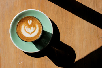Latte art in a cup on a wooden surface with sunlight and shadow.