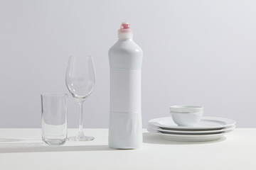 Dish washing bottle and ceramic plates and glasses organized on a flat surface on a white background, reflecting neatness and home care styling. Front view, mockup bottle for design label