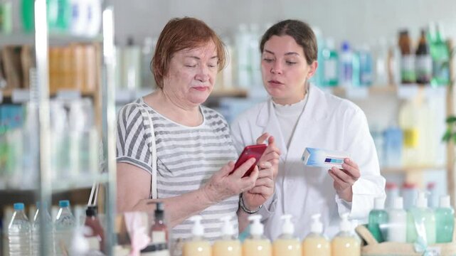 Elderly woman buyer scanning qr code for ointment with young woman pharmacist in pharmacy