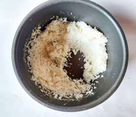 Top View of Leftover Steamed White Rice Sticking to Non-Stick Inner Pot of Rice Cooker After Cooking at Home