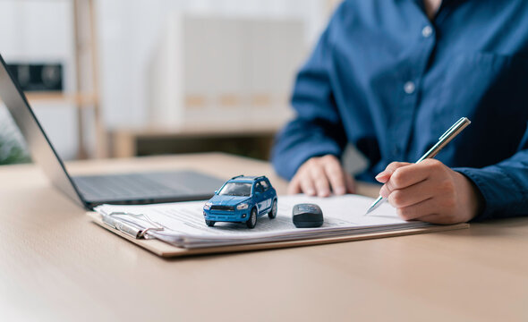 buyer signing vehicle registration papers on a clipboard with a laptop and miniature car on top, representing online car registration and ownership transfer