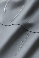 Close-up of waterproof ripstop fabric in dark gray with visible grid pattern, showing realistic water droplets and elongated streaks forming on the surface.