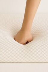 A close-up realistic photo of a human hand pressing firmly into a white memory foam mattress with a hexagonal texture, showing visible indentation and slow rebound effect. 