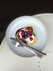 Russian Cheese Pancakes with Sour Cream, Fruit Jam, Raspberries, Blueberries, and Mint. Eating Out Breakfast Idea. Authentic Mobile Photo, Selective Focus, Non-AI