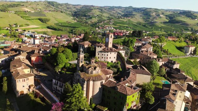 Historic hilltop village of Neive in Piedmont, Italy, ancient buildings, tower, and surrounding green landscape. Aerial drone backward