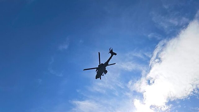 Rare slow motion footage of a United States military army Apache AH-64 helicopter flying over a battlefield with trenches during a sunny summer day in a pine forest in the Baltics europe. Silhouette.