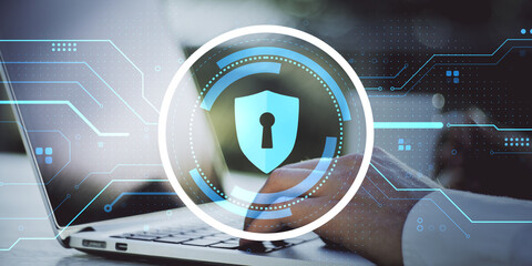 Cybersecurity concept with digital shield lock icon overlay on laptop screen and person typing in background, symbolizing data protection and privacy.