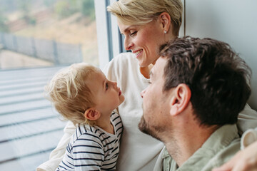 Obraz premium Parents playing with little son, sitting by window.