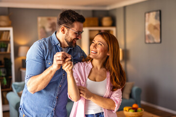 A couple is standing together, happily showing the key to their new home. The image captures...