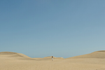 Woman Walking on Sand Dunes Under Blue Sky