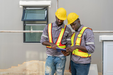 Two construction worker in a helmet and safety vest review plan on tablet at a building site. They...