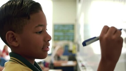 Intelligent African american school kid solving maths problem on a whiteboard in a classroom. Young confident student writing on a board during a lesson at school to practice mathematical equations - Powered by Adobe