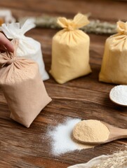 Bags of flour in various colors arranged on a wooden surface with a small wooden spoon