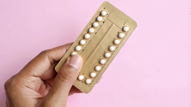 Hand Holding Oral Contraceptive Pills Blister Pack on Pink Background Showing Birth Control Method
