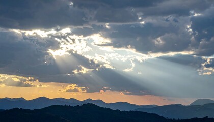 Sunbeams piercing a cloudy sky over hills