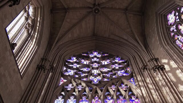 Gothic cathedral interior with ornate stained glass windows and intricate stone tracery illuminated by natural light

