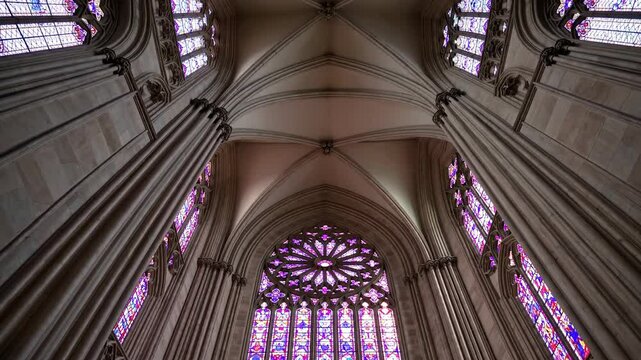 Gothic cathedral interior with tall arched columns, vaulted ceiling, and rose stained glass window in purple tones

