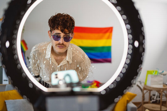 Influencer vlogging with mobile phone in front of rainbow flag at home