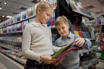 Little siblings buying plastic folder for copybooks at stationery store