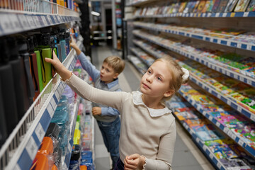 Cute schoolchildren doing shopping at stationery store walking through shelves
