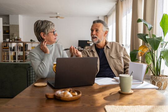 Senior couple discussing plans at home with a laptop and coffee